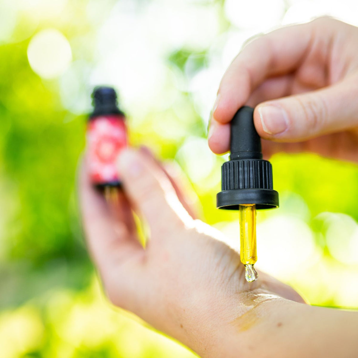 Applying oil from a dropper onto a wrist outdoors, a small red-labeled Lotuswei bottle blurred in the background